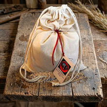 A small natural canvas drawstring pouch filled with 5lbs of Bineshii wild rice, tied with a red leather strap and  displayed on a rustic wooden table.