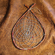 A rustic teardrop-shaped dreamcatcher with a weathered brown wooden hoop with sinew webbing, and red carved bone bead.